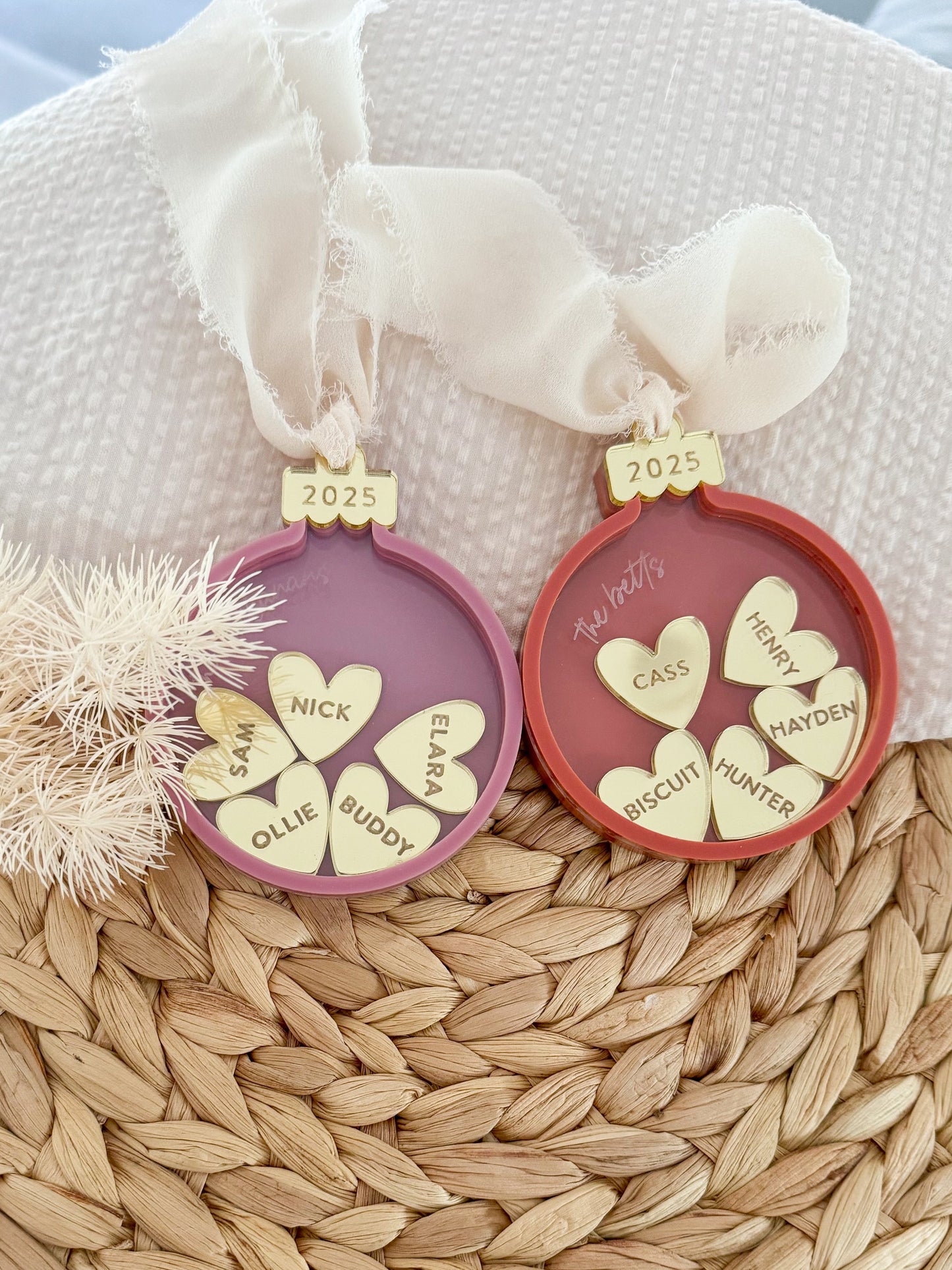 Two round acrylic baubles with 5 gold mirror hearts inside, engraved with family member's names. Features a frayed chifon ribbon and the top of the bauble says 2025.