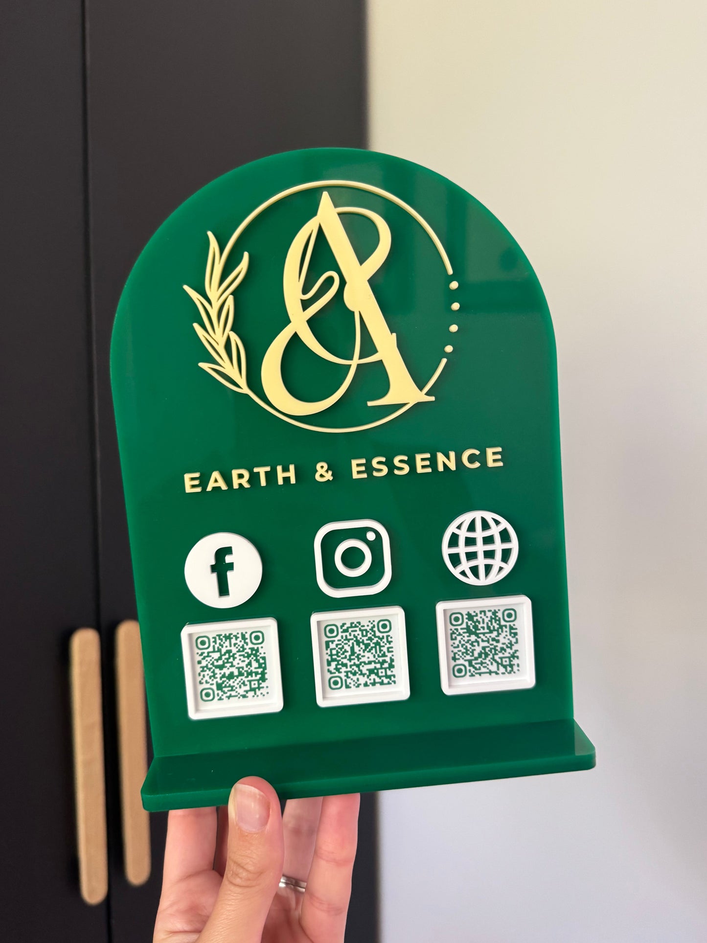 Green custom acrylic sign with brand logo and QR codes, held by a hand.