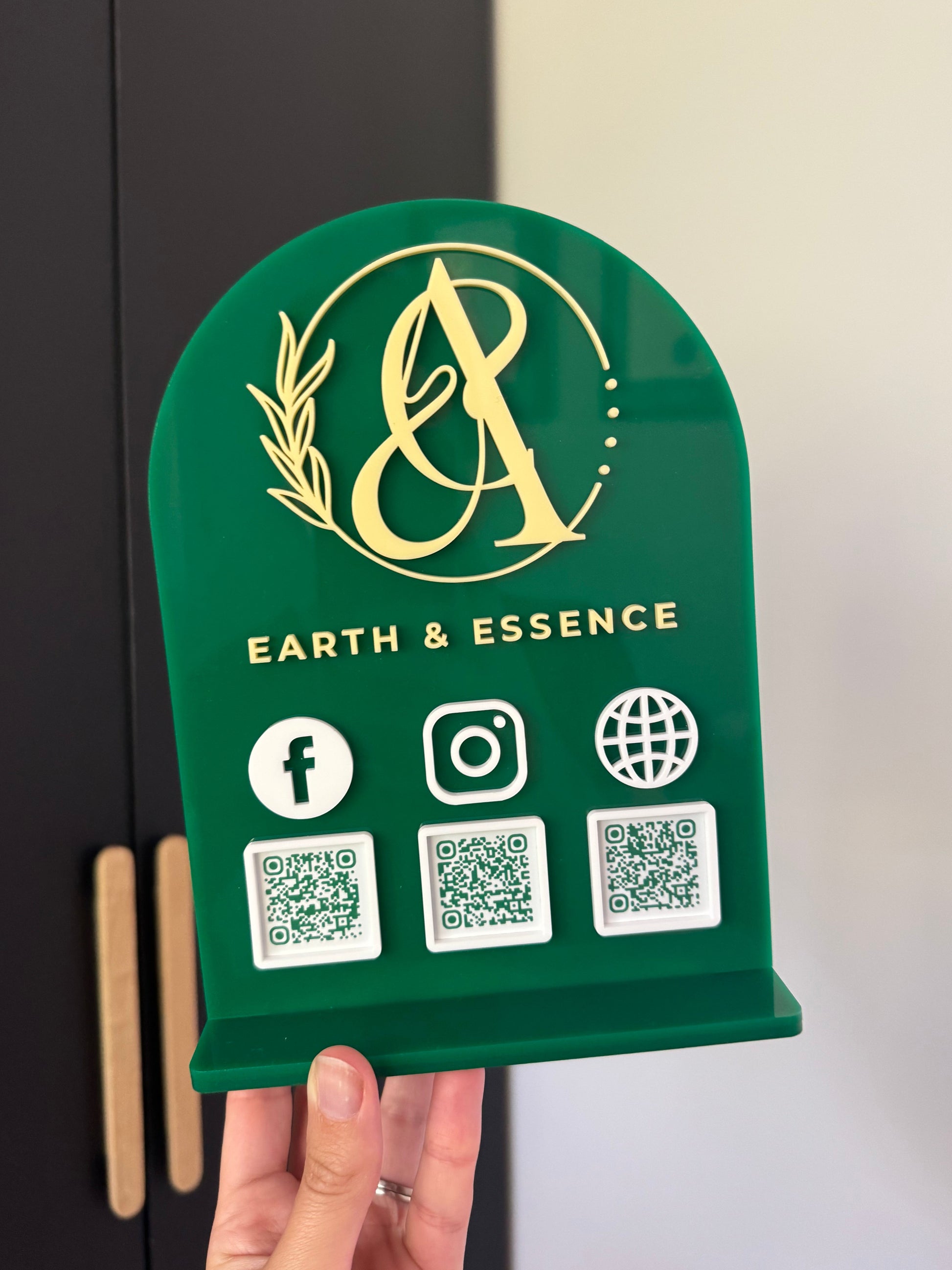 Green custom acrylic sign with brand logo and QR codes, held by a hand.